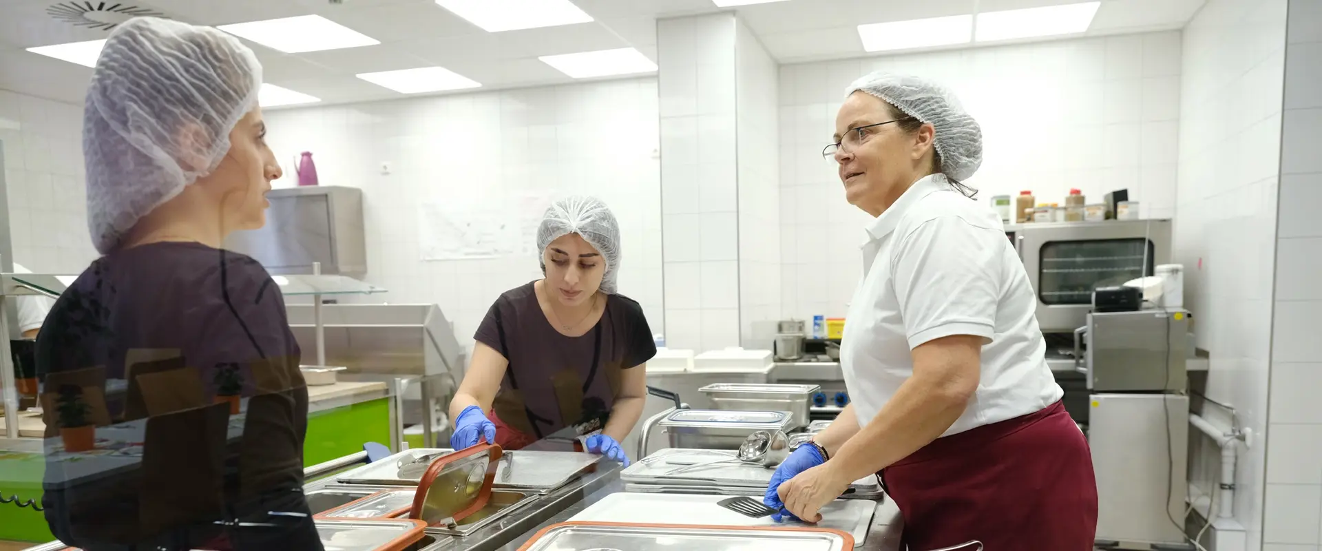 Zwei junge Frauen mit Migrationshintergrund und eine Fachanleiterin bereiten Essen zu