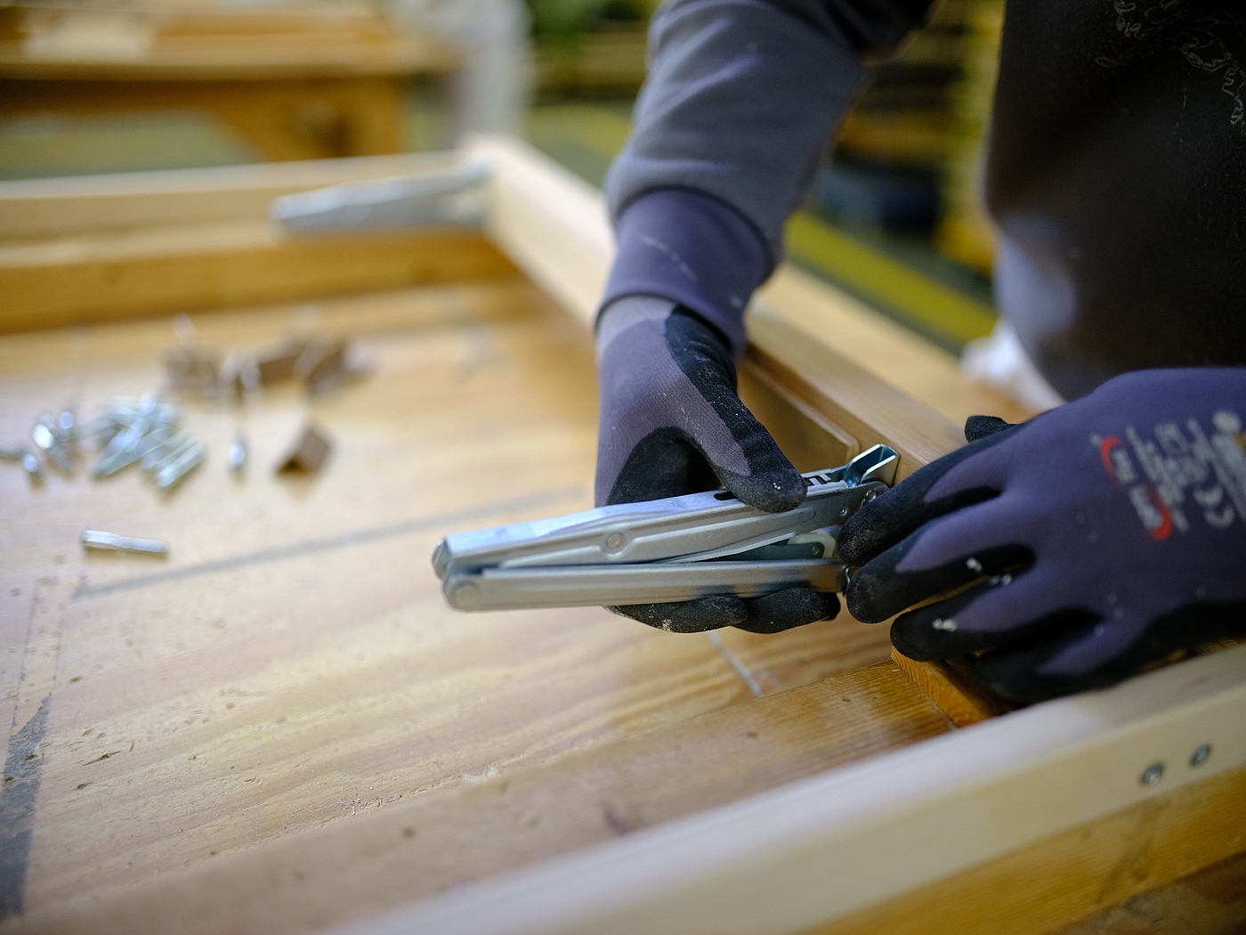 Metallwinkel werden an einen Lattenrost geschraubt, man sieht zwei Hände in blauen Handschuhen