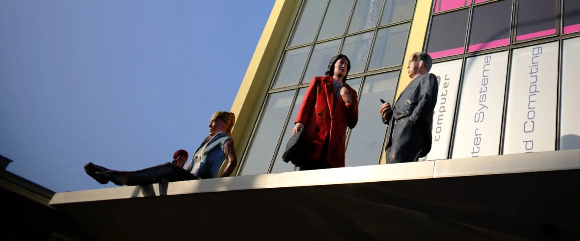 Gebäude des KuBa Campus von Außen. Gelbes Mauerwerk und viele hohe Fenster. Bunte Plakate und große Figuren verschiedener Menschen sind zu sehen